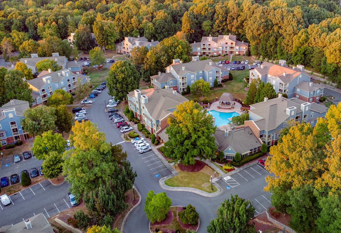 an aerial view of a large, busy residential area with numerous buildings arranged around a central pool, where many cars are parked in the parking lot