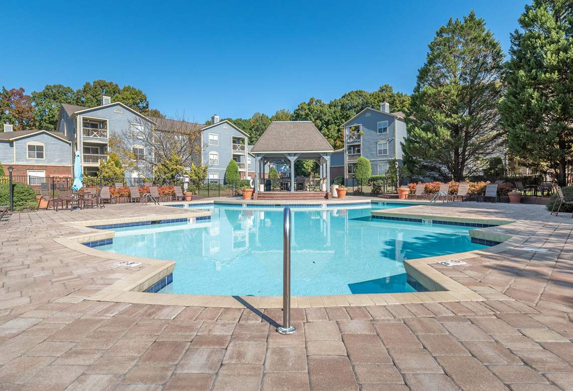 a vacant swimming pool surrounded by a deck and several potted plants